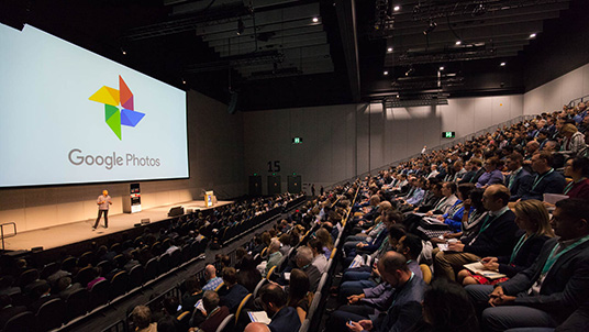lecturer talking to theatre of people with Google logo on screen