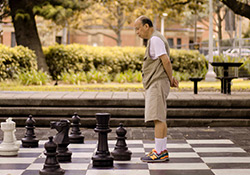 Man playing giant chess in a green courtyard