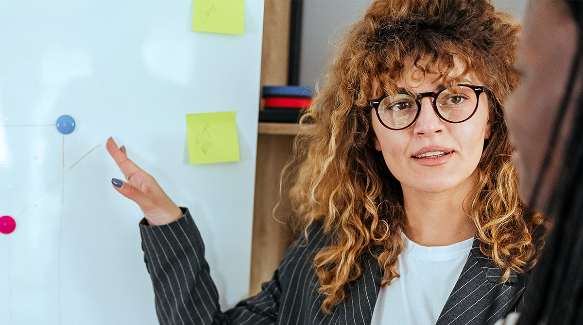 Woman at whiteboard, presenting to co-workers